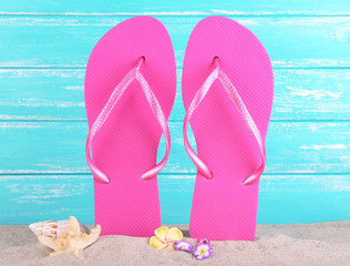 Bright flip-flops on sand, on wooden background