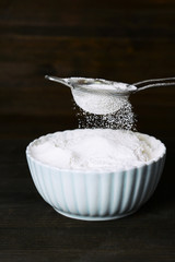 Sifting flour into bowl on table on wooden background