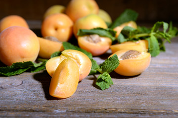 Ripe apricots with green mint leaves on wooden background