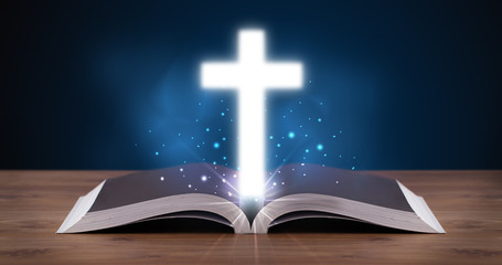 Open holy bible with glowing cross in the middle