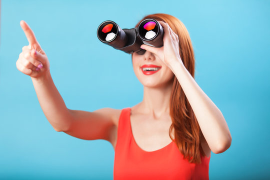 Redhead girl with binocular on blue background.