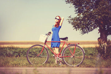 Fototapeta premium Redhead girl with bicycle on country road.