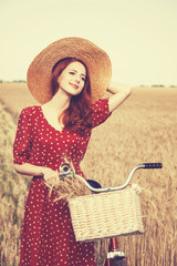 Redhead peasant girl with bicycle on wheat field.