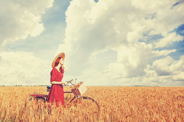 Redhead peasant girl with bicycle on wheat field.