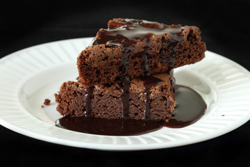 Slices of brownie on white plate covered with chocolate