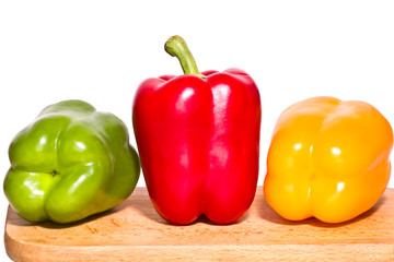Three bell peppers - green, red and yellow on a cutting board