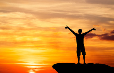 Fototapeta premium Silhouette of a man on a mountain top on fiery orange background