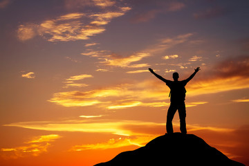 Silhouette of a man on a mountain top on fiery orange background