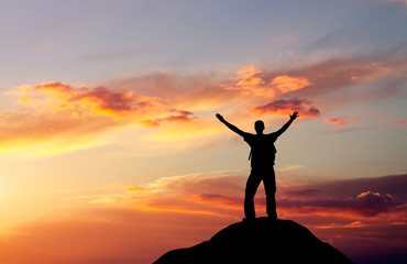Silhouette of a man on a mountain top on fiery orange background