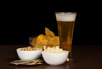 Glass of beer, bowl with chips, squids, pistachios