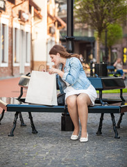 woman looking inside of white shopping paper bag on bench