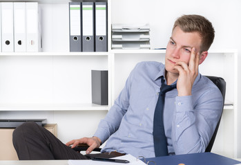 Fototapeta premium Junger nachdenklicher Mann sitzt am Schreibtisch im Büro