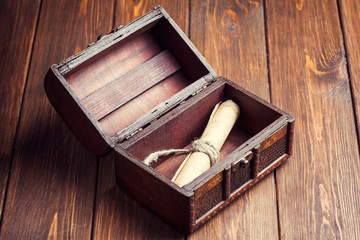 old paper roll inside treasure chest on wooden background