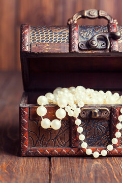 old treasure chest with pearl necklaces standing on wooden table