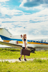 beautiful woman with old suitcase posing against plane