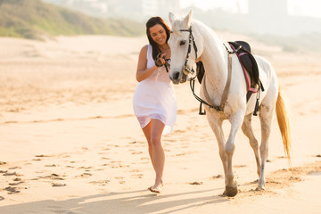 cheerful young woman walking with a horse on beach