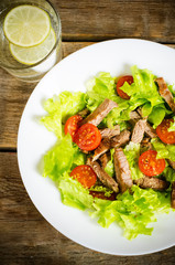 green salad with tomatoes and roast beef in a white dish