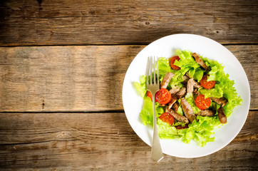 green salad with tomatoes and roast beef in a white dish