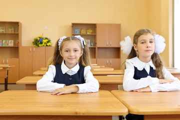 Two happy girls in uniform sit at wooden school desk