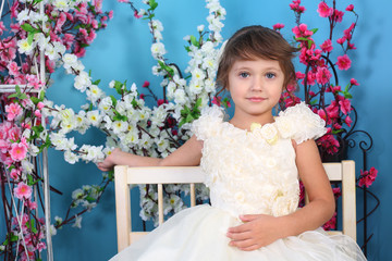 Beautiful little girl in white dress sits on bench in blue room