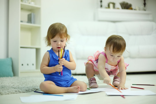 Two little cute girls paint pencils on floor in room at home.
