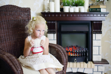 Little sad girl sits in wicker rocking chair with toy bear