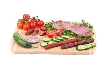 Sausage salami and vegetables on wooden platter.
