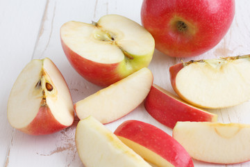 Pink lady apples cut on a painted white rustic wood table.