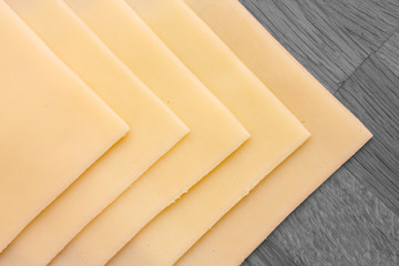 Sliced yellow cheese neatly arranged on wood surface. Above.