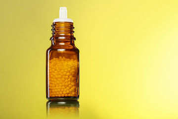 single bottle with homeopathy globules with yellow background