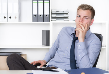 Junger nachdenklicher Mann sitzt am Schreibtisch im Büro