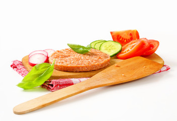 Raw burger patty and sliced vegetables