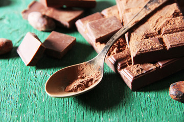 Cocoa powder and dark chocolate on color wooden background