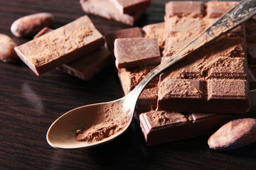 Cocoa powder and dark chocolate on color wooden background