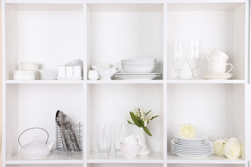 Different white clean dishes on wooden shelves