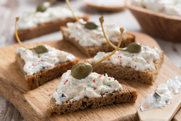 toasts with cheese pate and capers on a wooden board