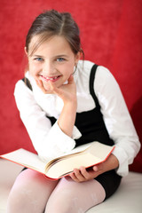 Uśmiechnięta dziewczynka czyta książkę - obrazy, fototapety, plakaty