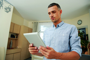 Handsome man standing and using tablet computer at home