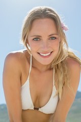 Beautiful blonde in white bikini smiling at camera on the beach