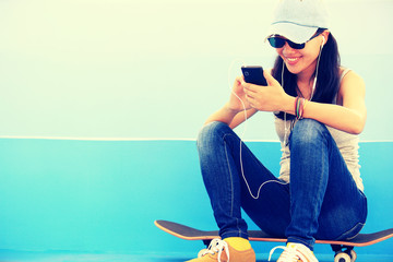 woman skateboarder listening music from smart phone mp3 player
