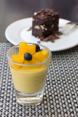 mango pudding in a glass and chocolate brownie as background, ca