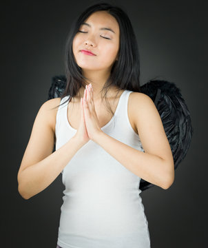 Asian young woman dressed up as an angel in prayer position with