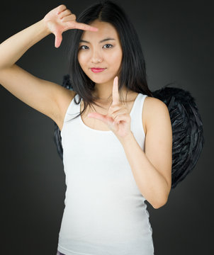 Asian young woman dressed up as an angel making frame with