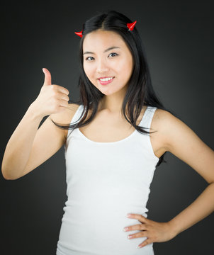 Asian young woman in devil horns showing thumb up sign and