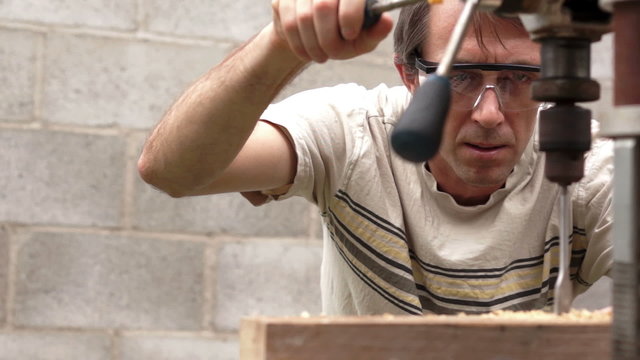 Man Using Drill Press On Wood Board