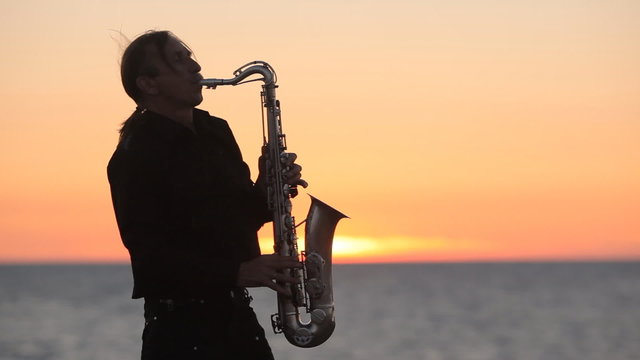 The silhouette of a musician playing saxophone on the seacoast