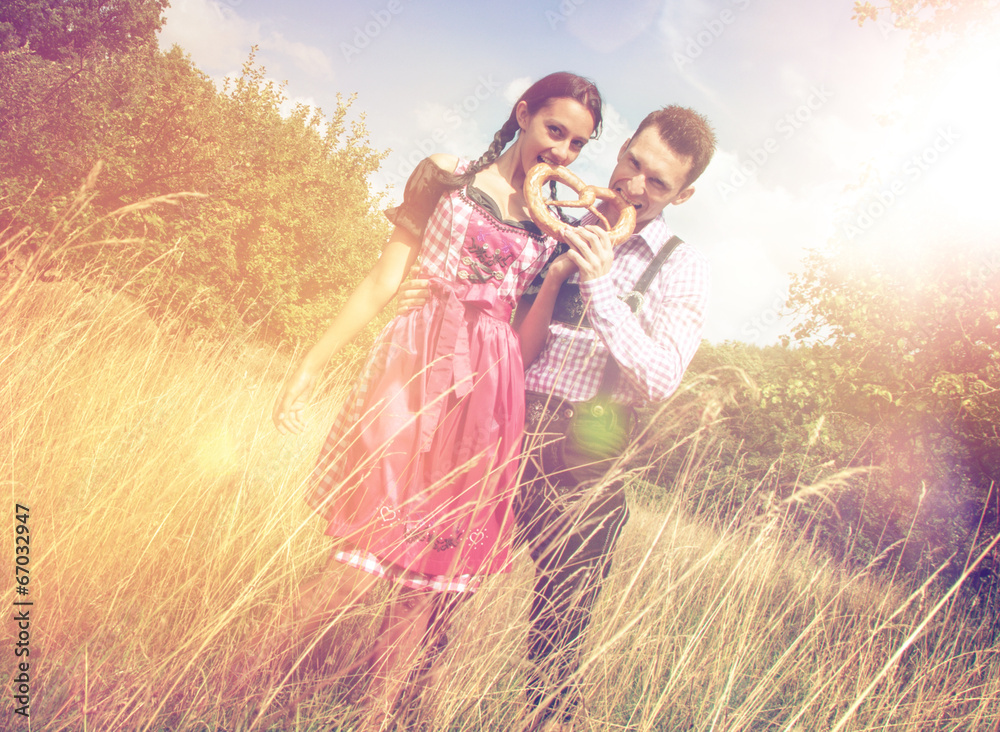 Wall mural Couple in Bavarian clothes eat a brezel outside