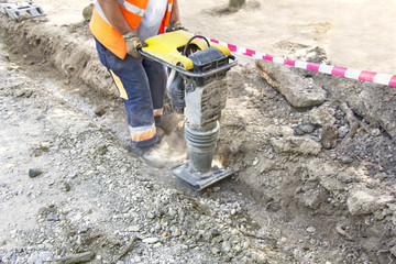 Worker uses compactor to firm soil at worksite - obrazy, fototapety, plakaty