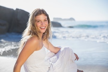 Fototapeta na wymiar Beautiful smiling blonde in sundress sitting on the beach