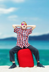Fototapeta premium Boy sitting with his luggage at the beach and screaming